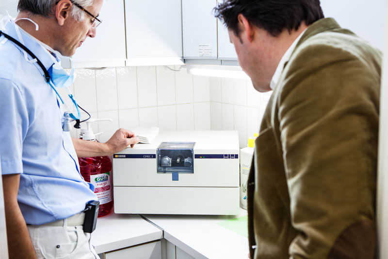 Dr. Wilmes zeigt einem Patienten das CEREC-Gerät zur Herstellung von Zahnkronen direkt in der Praxis.
